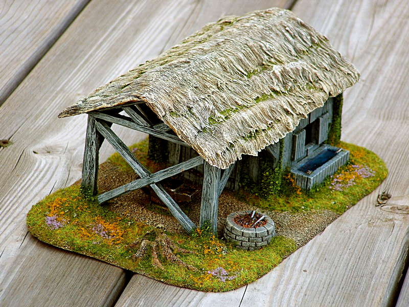 Finished miniature blacksmith shop with a weathered thatched roof, timber work area, stone well and overgrown scenic base